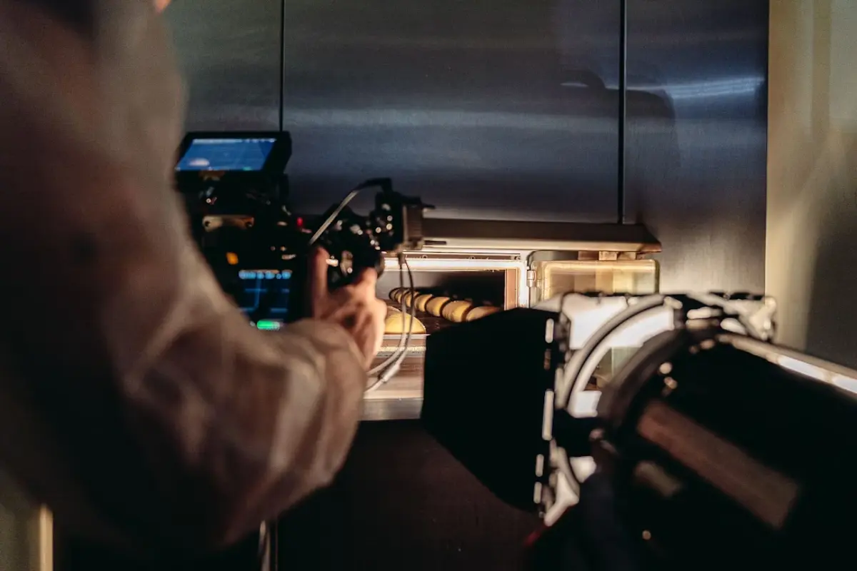 This is a photograph taken behind the scenes of a food production or commercial shoot, likely in a professional kitchen environment. The image is focused on the intense process of filming food.
