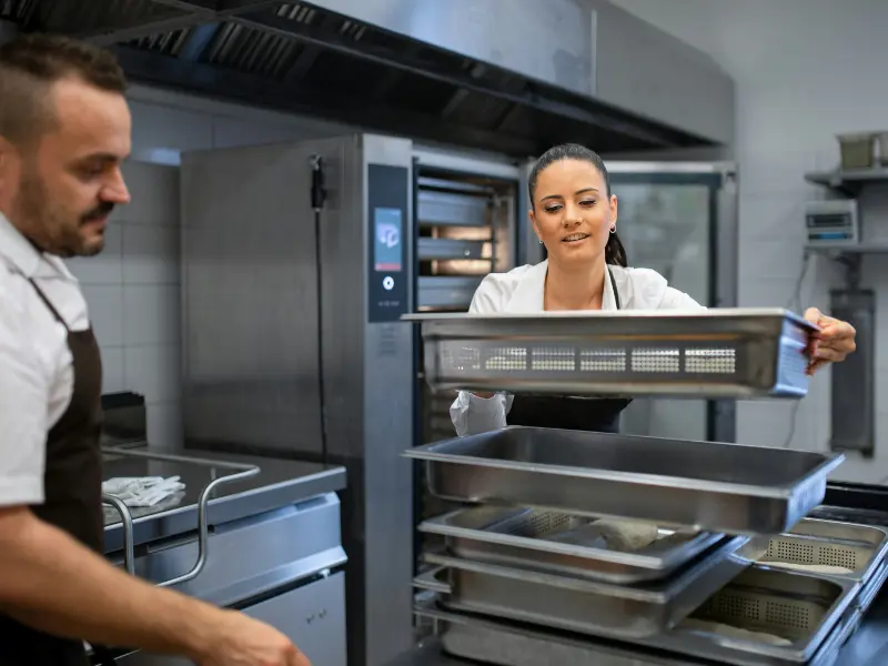This photo shows a man and a woman working together in a professional kitchen. They both appear to be chefs or kitchen staff.